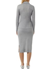 Grijs lange mouw top met een mock neck, in combinatie met een grijze gebreide rok met zijsplitten. Het materiaal is glad en aansluitend. Zilveren platte schoenen.