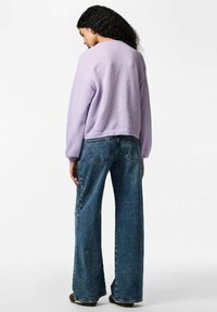 Lilla strikkegenser med avslappet passform og lange ermer, kombinert med høytlivede, vide blå jeans med falmet denimuttrykk.