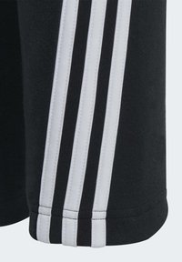 Pantalones cortos deportivos negros con tres franjas blancas en los laterales, cinturilla elástica y una suave tela de mezcla de algodón con detalles de costura visibles.