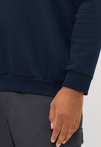 Navyblaues Sweatshirt mit gerippten Bündchen und Saum. Weiches Baumwollmaterial, lockere Passform, detaillierte Nähte an den Ärmeln und am Handgelenk sichtbar.