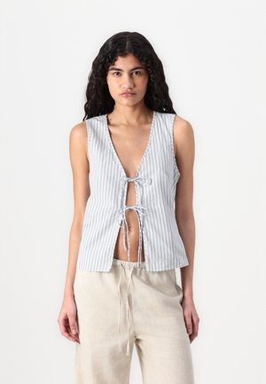 Striped sleeveless top in light gray and white, featuring a deep V-neck and front tie closure, paired with relaxed linen pants.