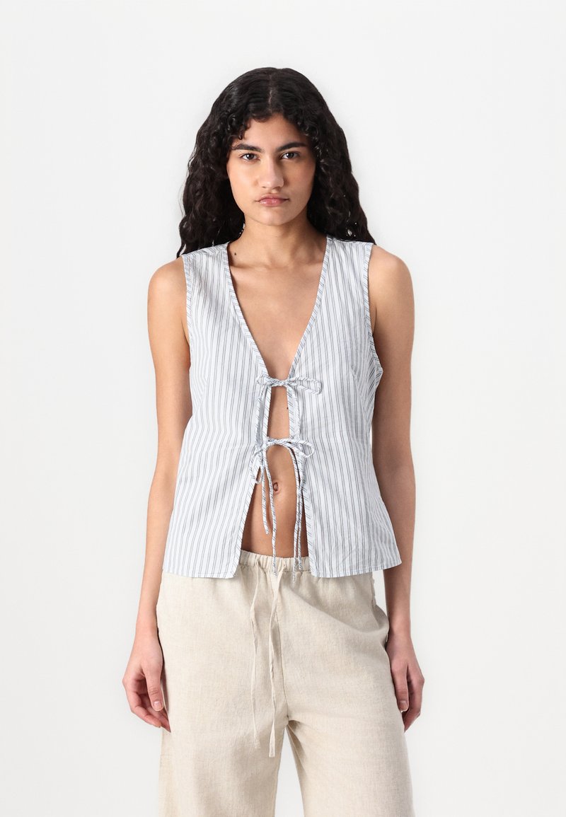Débardeur rayé sans manches en gris clair et blanc, doté d'un décolleté en V plongeant et d'une fermeture à lien à l'avant, associé à un pantalon en lin décontracté.