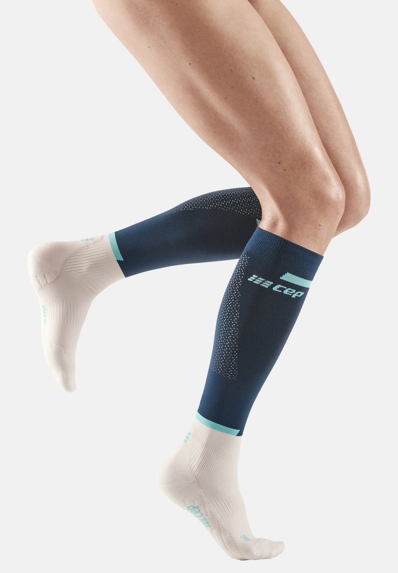 Blauwe en witte compressiekousen met een gestructureerd ontwerp, voorzien van een teal accentband en reflecterend logo-detail op de kuit.