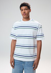 Maglietta bianca in cotone con strisce orizzontali in blu scuro, azzurro e verde. Vestibilità comoda con scollo rotondo e maniche corte.