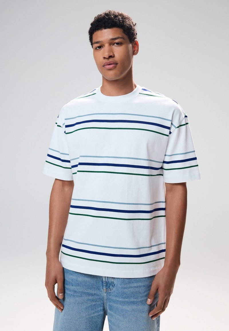 Maglietta bianca in cotone con strisce orizzontali in blu scuro, azzurro e verde. Vestibilità comoda con scollo rotondo e maniche corte.