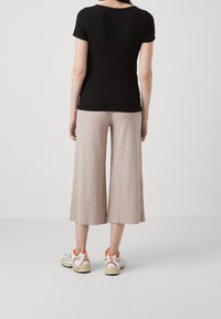 Černý žíhaný krátký rukáv top spojený se světlými béžovými žíhanými širokými nohavicemi a bílými teniskami s oranžovými akcenty.