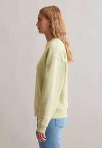 Lichtgroene sweatshirt met een ronde hals, verlaagde schouders en ribgebreide manchetten. Heeft een klein wit logo op de achterkant.