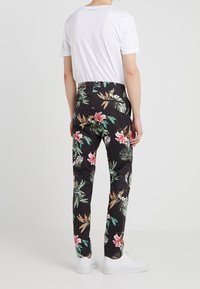 Schwarze Blumenhose mit lebhaften rosa und grünen tropischen Mustern, aus glattem Stoff, kombiniert mit einem weißen T-Shirt und weißen Schuhen.