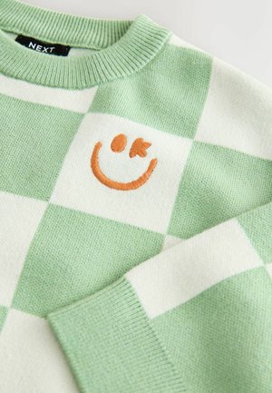 Zielono-biały sweter w kratę z ribbingu przy szyi. Posiada haftowaną pomarańczową uśmiechniętą buźkę na klatce piersiowej. Miękka struktura dzianiny.