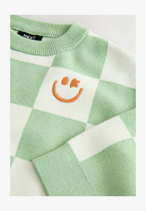 Pull en maille à carreaux verts et blancs avec un col côtelé. Présente un smiley orange brodé sur la poitrine. Texture en maille douce.