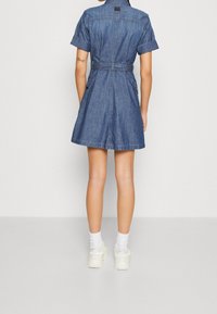 Jeanskjol med korta ärmar, cinchad midja, två sidofickor och en utsvängd nederkant, med en ryggsöm och sömdetaljer.