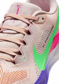 Jasnoróżowy but biegowy Nike z jasno-pomarańczowymi sznurówkami, jaskrawozielonym logo i podeszwą z gradientem fioletu i różu. Napis "No Human is Limited."