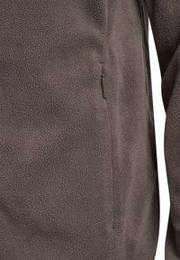 Detailaufnahme einer braunen Fleecejacke mit weichem, strukturiertem Stoff und einer vertikalen Reißverschlusstasche an der Seite mit Stoff-Zuglasche.