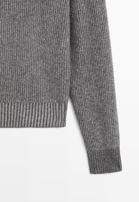 Pull en tricot gris avec un motif texturé, doté de poignets et d'un ourlet côtelés. Le matériau semble doux et chaud, idéal pour le temps frais.