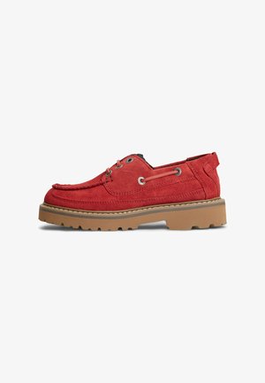 Zapato náutico de ante rojo con suela gruesa de goma marrón claro, detalles de cordones a los lados y diseño cosido en la puntera tipo mocasín, mostrado de perfil sobre fondo blanco.