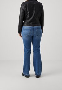 Zwarte leren jas en blauwe wijde jeans. Details zijn onder andere achterzakken en een rafelige zoom aan de jeans. Gladde textuur van de jas, casual uitstraling.