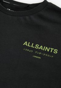 Melna kokvilnas t-krekls ar zaļu "ALLSAINTS" logo un papildus tekstu japāņu un angļu valodā. Ar ribotu apļa kakla dizainu.