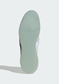 Sohle aus hellgrünem Gummi mit strukturierter Griffmuster, in runder Form. Der obere Teil zeigt schwarz-weiße Akzente.