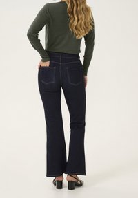 Mörkblå utsvängda jeans med fem fickor, sömnadsdetaljer och hög midja, tillsammans med en mörkgrön kortärmad tröja.