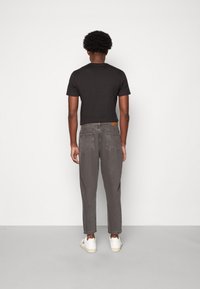 Czarny t-shirt z krótkim rękawem i okrągłym dekoltem, zestawiony z szarymi zwężanymi dżinsami. Na pasie znajduje się skórzana metka.