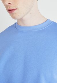 Sudadera de algodón azul con cuello redondo acanalado. Textura suave, tejido ligero, con un color sólido sin patrones ni detalles.