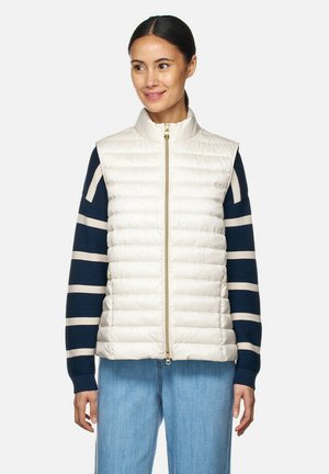 Gilet matelassé blanc cassé, avec une texture en matelassé, un col haut et une fermeture éclair dorée, associé à un haut à rayures marines à manches longues et à un jean bleu.