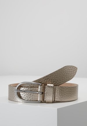 Teksturowany pasek z metalicznej skóry z zaokrągloną srebrną klamrą, ułożony płasko na białej powierzchni na tle jednolitego szarego tła.