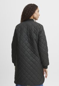 Schwarze, gesteppte Jacke mit langem Schnitt, die eine glatte Textur, gerippte Bündchen und ein Rautenmuster auf dem Stoff aufweist.