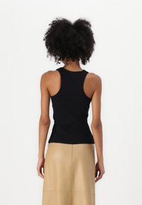 Melnas ribotās topiņš ar pieguļošu dizainu un platām rokām, kombinēts ar beidžu midi svārkiem, skatīts no aizmugures.