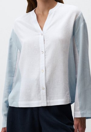 Femme portant une chemise à manches longues avec devant blanc et manches et côtés bleu clair, assortie à un pantalon foncé.