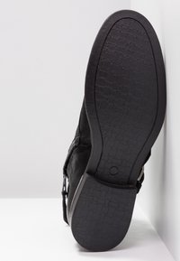 Black, textured shoe bottom with a patterned sole; features a smooth upper and a side zipper for easy wear.