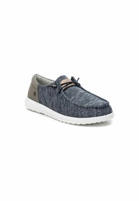 Zapatos de lona azul marino tipo slip-on, confeccionados con tela texturizada y acentos en gris claro, con una suela de caucho blanca; presentan cordones elásticos y un detalle de logo.