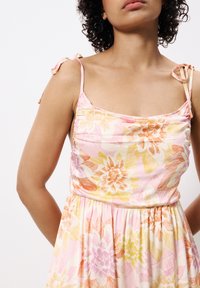 Robe fleurie dans des tons de rose, jaune et orange, dotée d'un corsage froncé, de bretelles spaghetti avec liens, et d'une jupe évasée fluide.