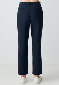 Marineblauwe op maat gemaakte broek met een gladde textuur, rechte pijpen, en twee achterzakken, gecombineerd met witte sneakers.