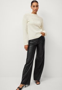 Suéter crema con cuentas texturizadas en el frente, cuello redondo y puños acanalados. Pantalones de cuero negros de pierna ancha con un acabado suave.