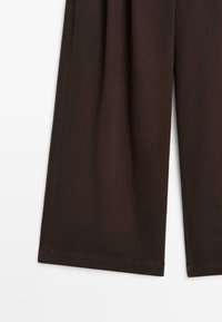 Donkerbruine wijde broek met zichtbare zijnaad en rechte zoom op een witte achtergrond, ingekort om alleen de onderbenen te tonen.