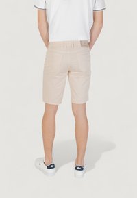 Pantaloni beige realizzati in tessuto leggero, con frontale piatto, tasche sul retro e etichetta in vita. Abbinati a sneakers bianche con dettagli blu navy.