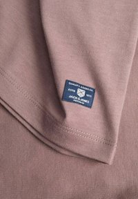 Camiseta de tela suave y acanalada en tono malva con una etiqueta de marca azul que dice "QUALITY GOODS CO. ESTD 1975 JACK & JONES PREMIUM".