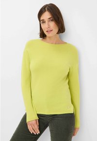 Limettengrüner Strickpullover mit langen Ärmeln, weitem Halsausschnitt und seitlichen Schlitzen, mit einem kleinen silbernen Logo am Saum.