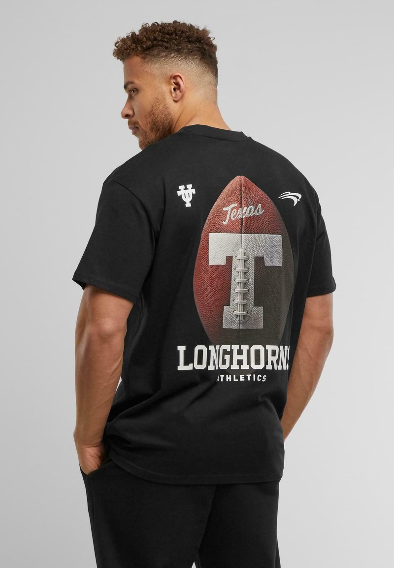 Juodas trumpomis rankovėmis marškinėliai su dideliu tekstūriniu futbolo grafiku, tekstu "Texas" ir tuo pačiu "LONGHORN ATHLETICS" ryškiu baltu šriftu.
