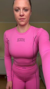 Lyserød atletisk langærmet top med tætsiddende design og logo, kombineret med matchende højtaljede leggings med kontrasterende sømme.