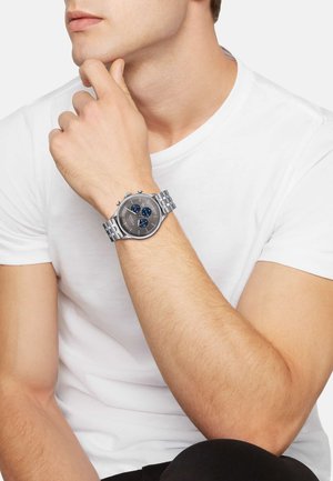 Sølv rustfrit stål ur med en rund grå urskive og to blå underskiver, udstyret med et metal link armbånd og tre trykknapper.