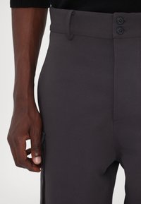 Sötétszürke nadrág sima textúrával, két gombbal a deréknál és oldalsó zsebekkel a funkciókérdés további növelése érdekében.