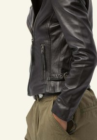 Czarna skórzana dopasowana kurtka z zamykanymi na zamek kieszeniami, gładką fakturą i dopasowanym krojem. Nosiowana na oliwkowe spodnie o luźnym kroju.