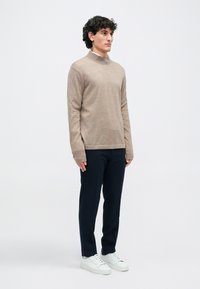 Beige hosszú ujjú pulóver magas gallérral, sötétkék nadrággal és fehér sportcipővel párosítva. Sima textúra, laza szabás.