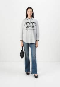 Gråstripet skjorte med svart "JOOP! JEANS" trykk, kombinert med blå vide jeans med teksturdesign og svart håndveske. Sorte sko.