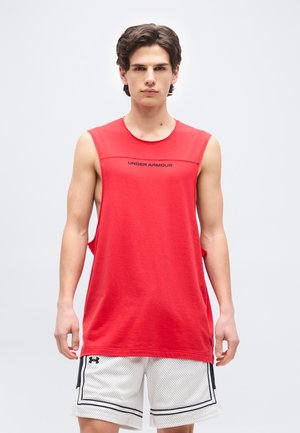Junger Mann trägt ein ärmelloses rotes Unter Armour Shirt und weiße Mesh-Basketballshorts, steht vor einem schlichten hellen Hintergrund.