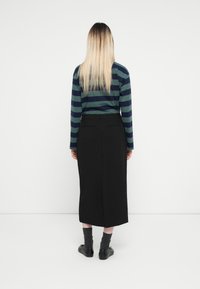 Haut à rayures à manches longues en vert et marine, assorti à une jupe noire mi-longue, à coupe droite et avec de subtils fentes au dos. Chaussures noires et chaussettes grises.