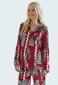 Punavaa satin-pyjama-setti, jossa on leopardikuosisuunnittelu mustilla ja valkoisilla yksityiskohdilla. Paidassa on tasku ja se on rennosti istuva pitkähihainen.