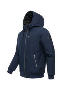 Mørkeblå hettejakke med glidelås foran, ribbede mansjetter og midje. Har et svart logo-patch på venstre erme og to sidelommer med glidelås.